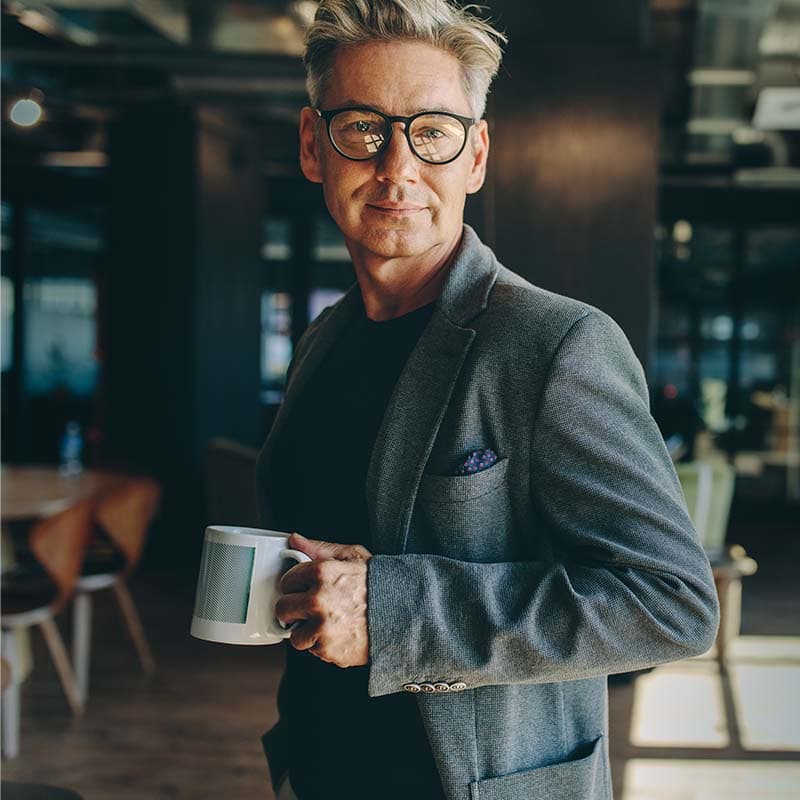 A white man wearing glasses looking at camera holding a coffee in his hands